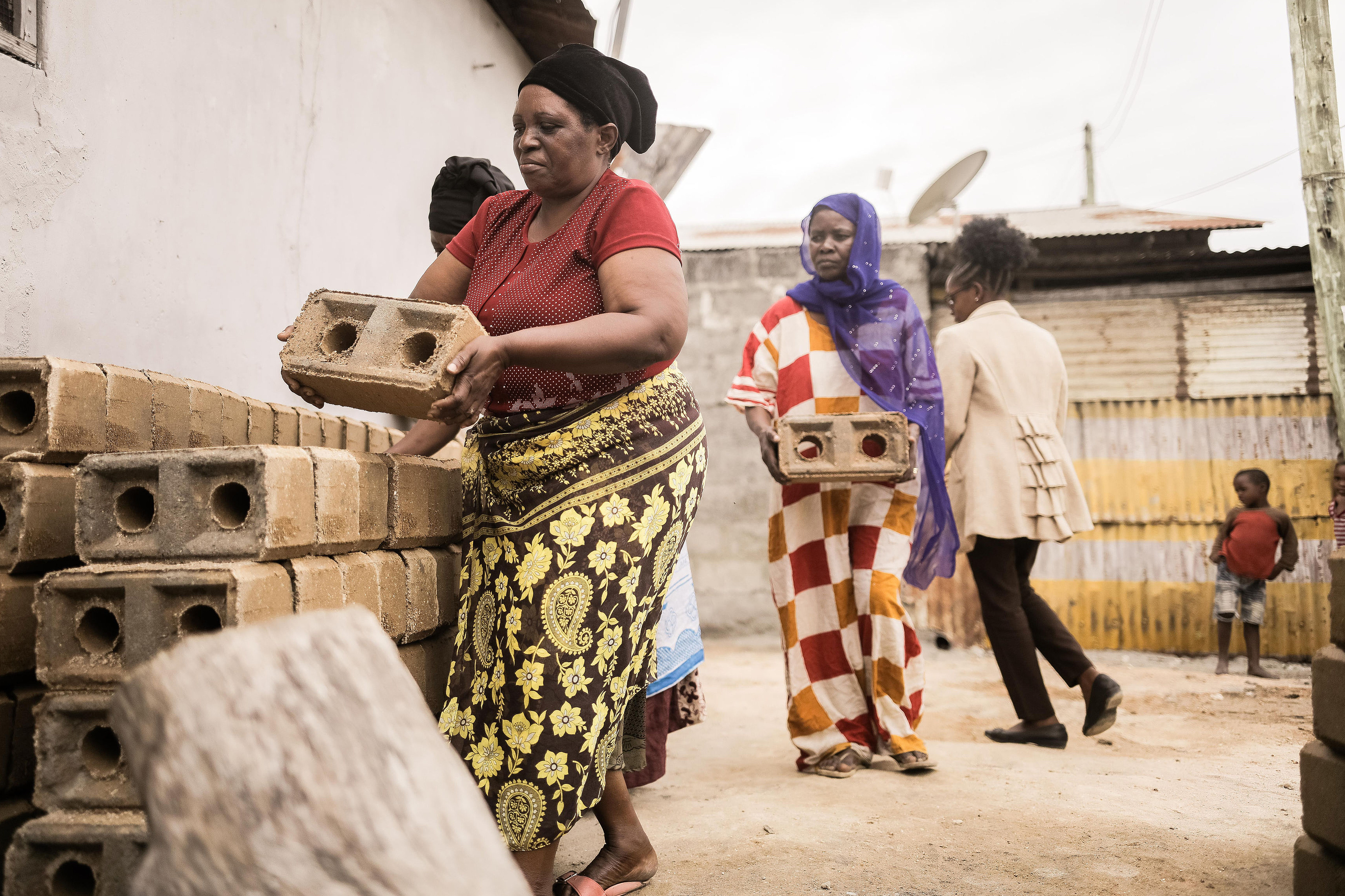 Frauen in bunter Kleidung stapeln Ziegelsteine.