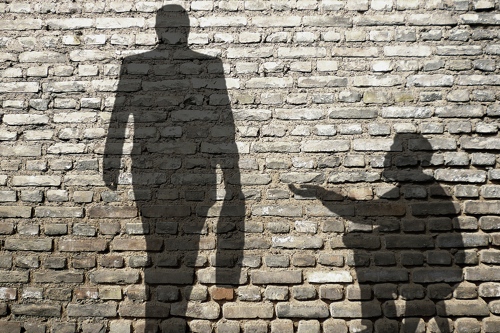 Schatten eines bettelnden Bettlers und eines Geschäftsmannes zeichnen sich an einer Mauer ab