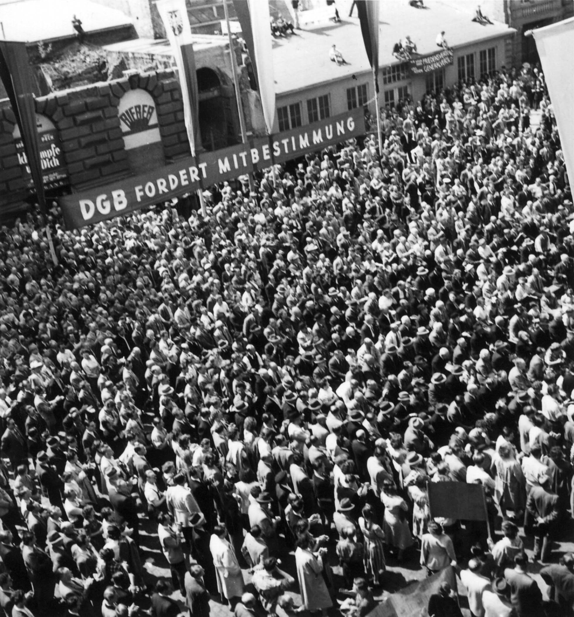 Schwarz-Weiß Fotografie von Menschenmenge bei Kundgebung, im Hintergrund Transparent "DGB fordert Mitbestimmung"