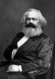 Eine Portraitfotographie von Karl Marx, gehalten in schwarz-weiß. Zu sehen ist nur der Oberkörper des sitzenden Karl Marx.