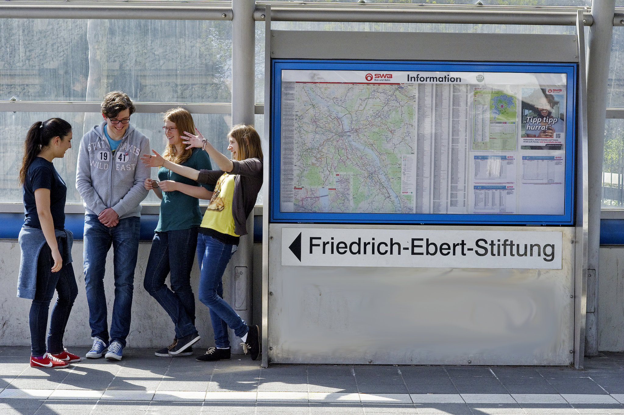 Menschen stehen an einer Straßenbahnhaltestelle. Dort zu sehen ist der Schriftzug: Friedrich-Ebert-Stiftung.