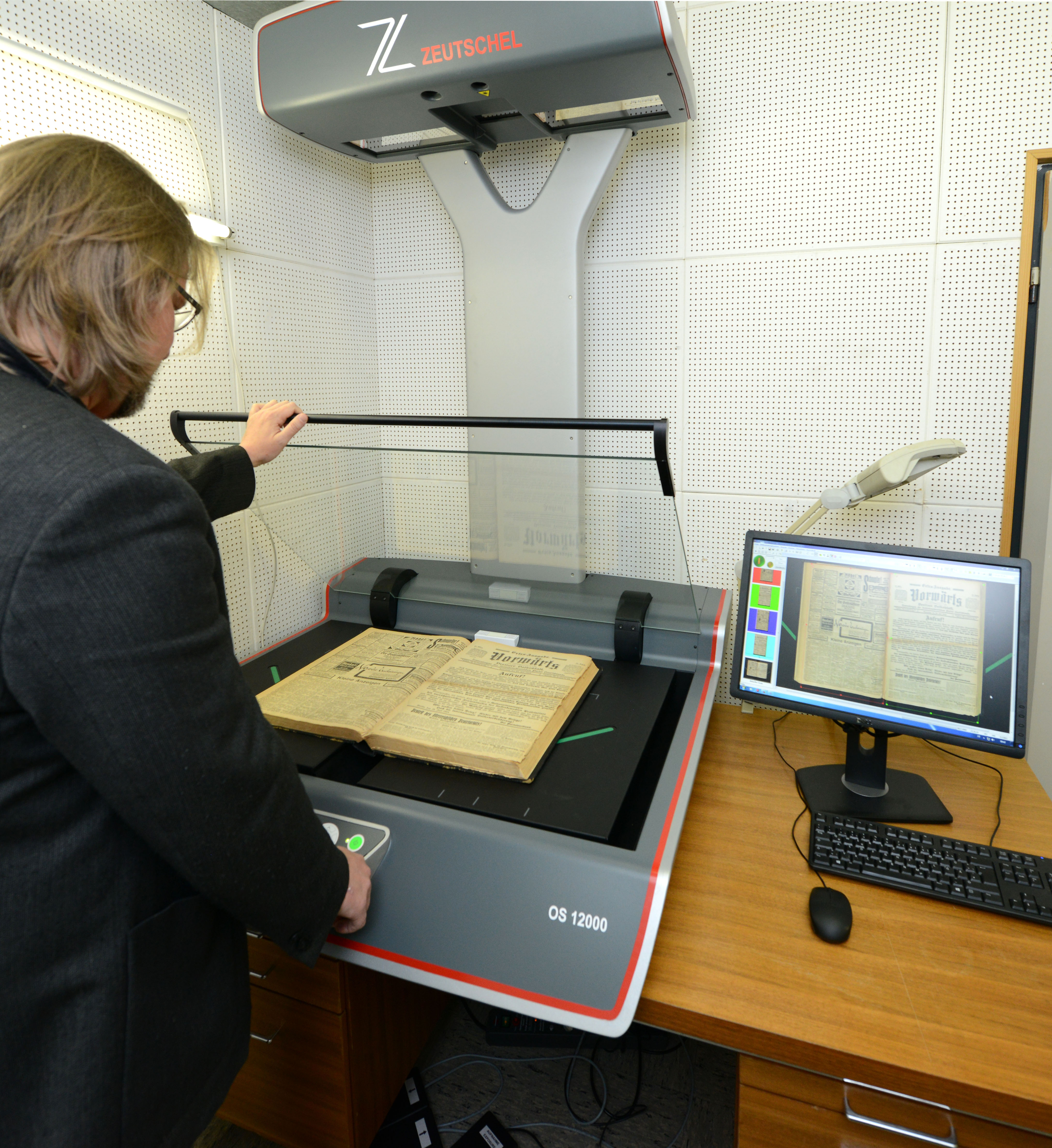 Ein Mitarbeiter der FES steht vor einem Scanner und digitalisiert ein altes Buch. 