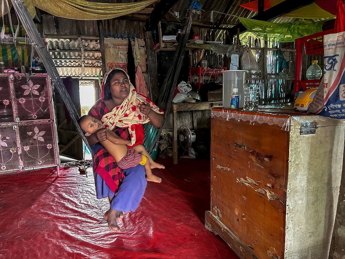 Auf dem Bild sieht man Rahima, eine Frau aus Bangladesh auf einer Hängematte in einer einfachen Hütte sitzen