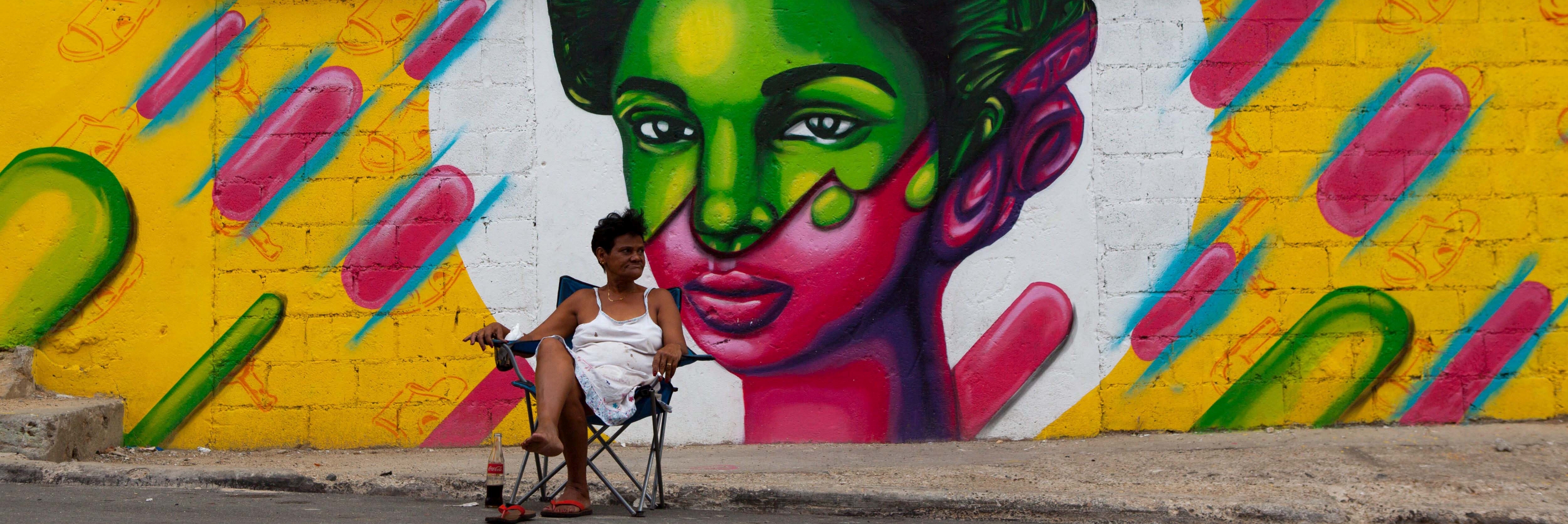 Sitzende Frau vor Graffiti eines Frauenporträts in der Dominikanischen Republik