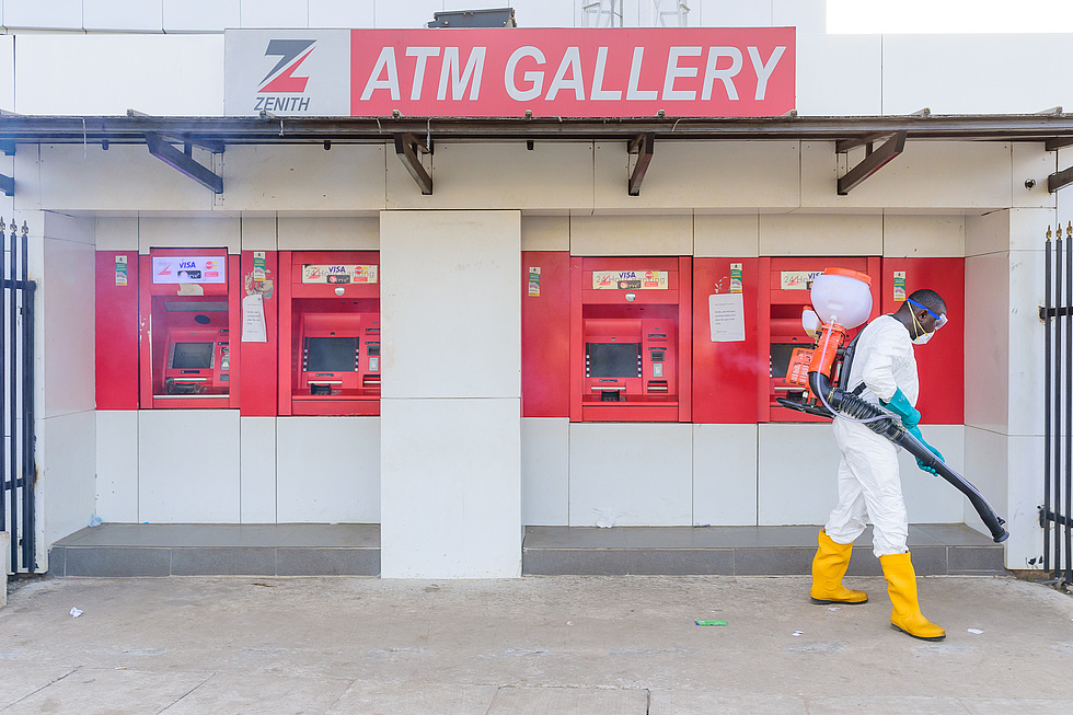Geldautomaten in Nigeria. Ein Mann in Schutzkleidung säubert den Boden mit einem Laubbläser