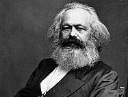 Eine Portraitfotographie von Karl Marx, gehalten in schwarz-weiß. Zu sehen ist nur der Oberkörper des sitzenden Karl Marx.