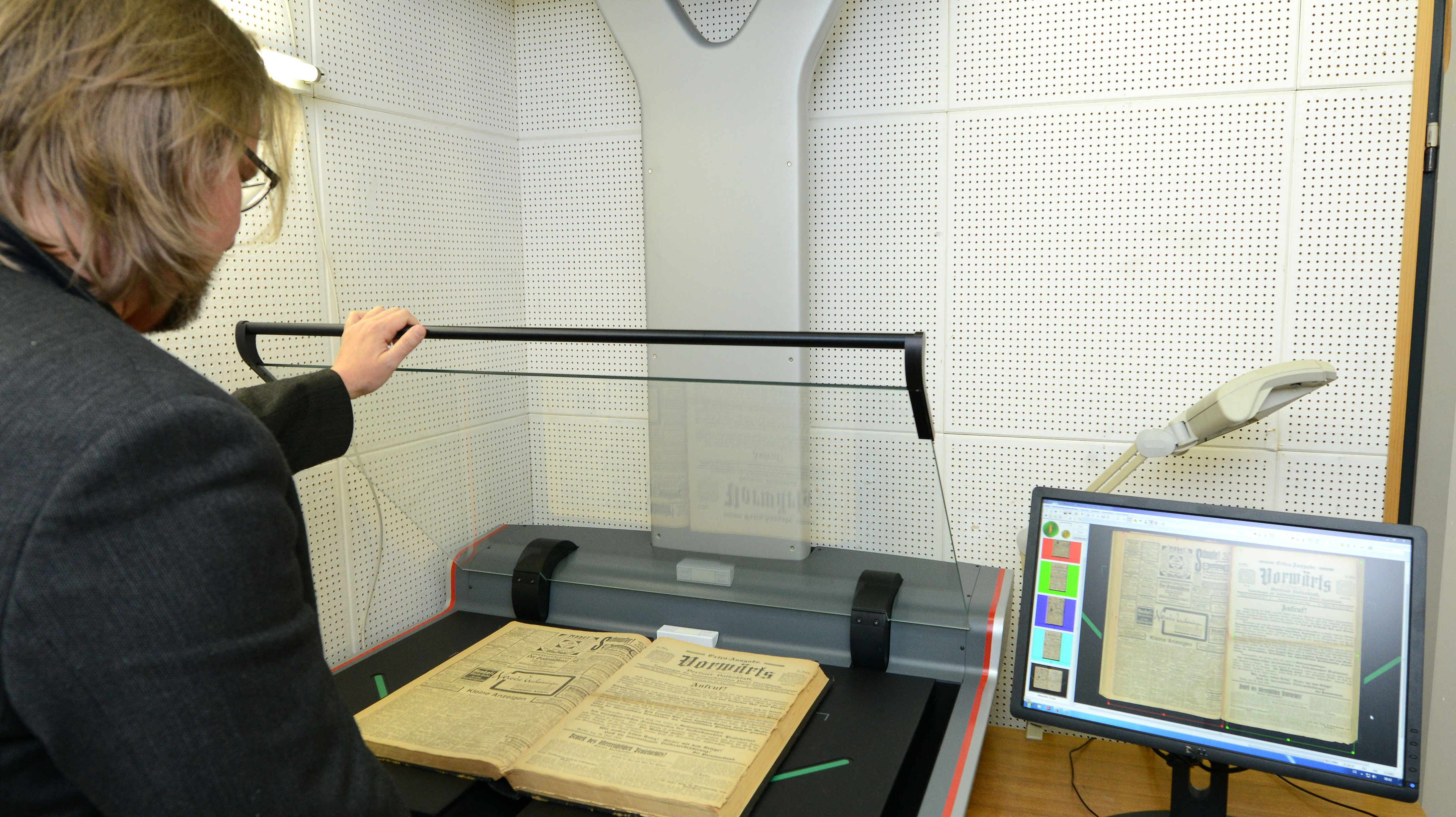 Ein Mitarbeiter der FES steht vor einem Scanner und digitalisiert ein altes Buch. 