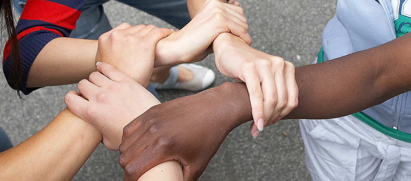 Fünf junge Menschen reichen sich die Hände mit unterschiedlicher Hautfarbe.