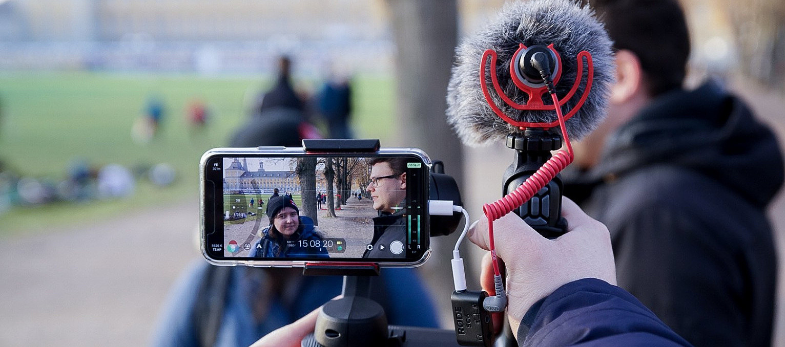 Ein Smartphone mit aufgestecktem Mikrofon filmt eine Person, die interviewt wird.