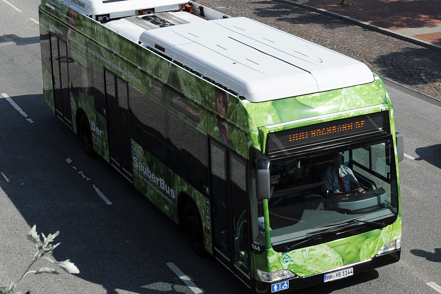 Vordergrund: HVV-Bus auf Straße; Hintergrund: Hamburger Hafen mit Elbphilharmonie