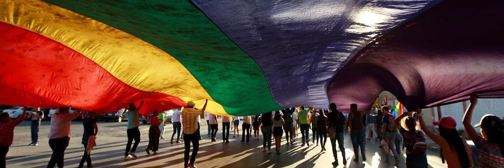 Menschen laufen unter einer riesigen Regenbogenfahne Richtung Sonne