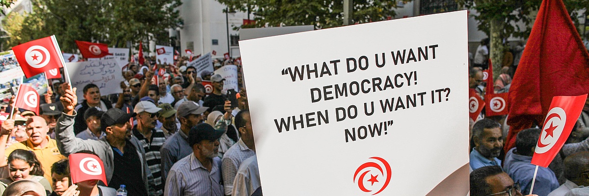 Demonstranten in einer Straße in Tunis mit einem Plakat mit der Aufschrift "What do you want? Democracy! When do you want it? Now!"