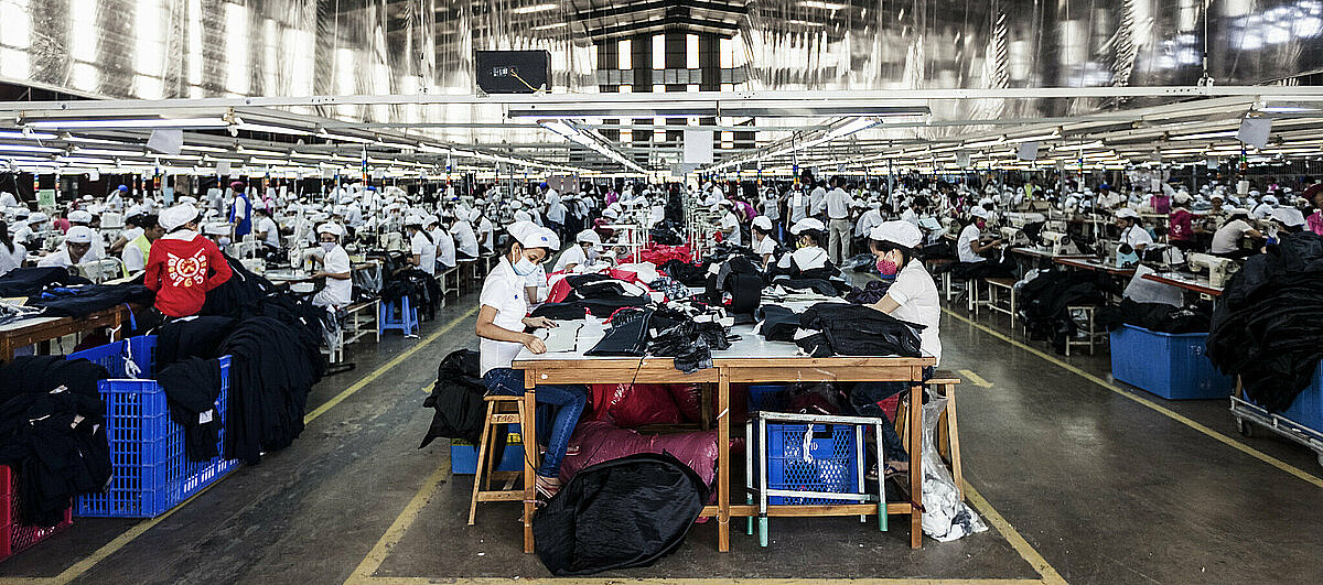 Arbeitende Asiaten*Innen in Schutzkleidung in einer Fabrikhalle der Textilindustrie.