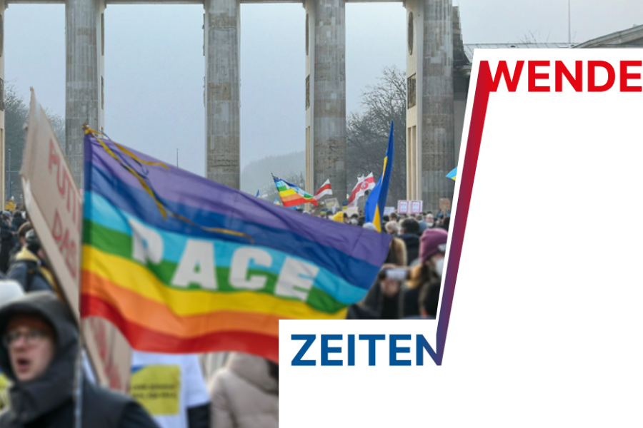 Eine Traube an Menschen demonstrieren vor dem Brandenburger Tor. In der Mitte des Bildes steht ein Demonstrant mit einer Pace-Fahne. Der Schrifzug "Zeiten - Wende" ist als Grafik zu lesen.