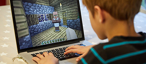 Junge sitzt am Laptop und spielt Minecraft.