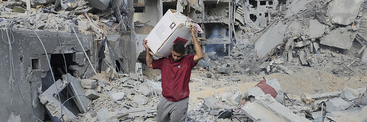 Ein Mann mit einem Karton auf der Schulter läuft über Trümmer in einem zerbombten Stadtviertel