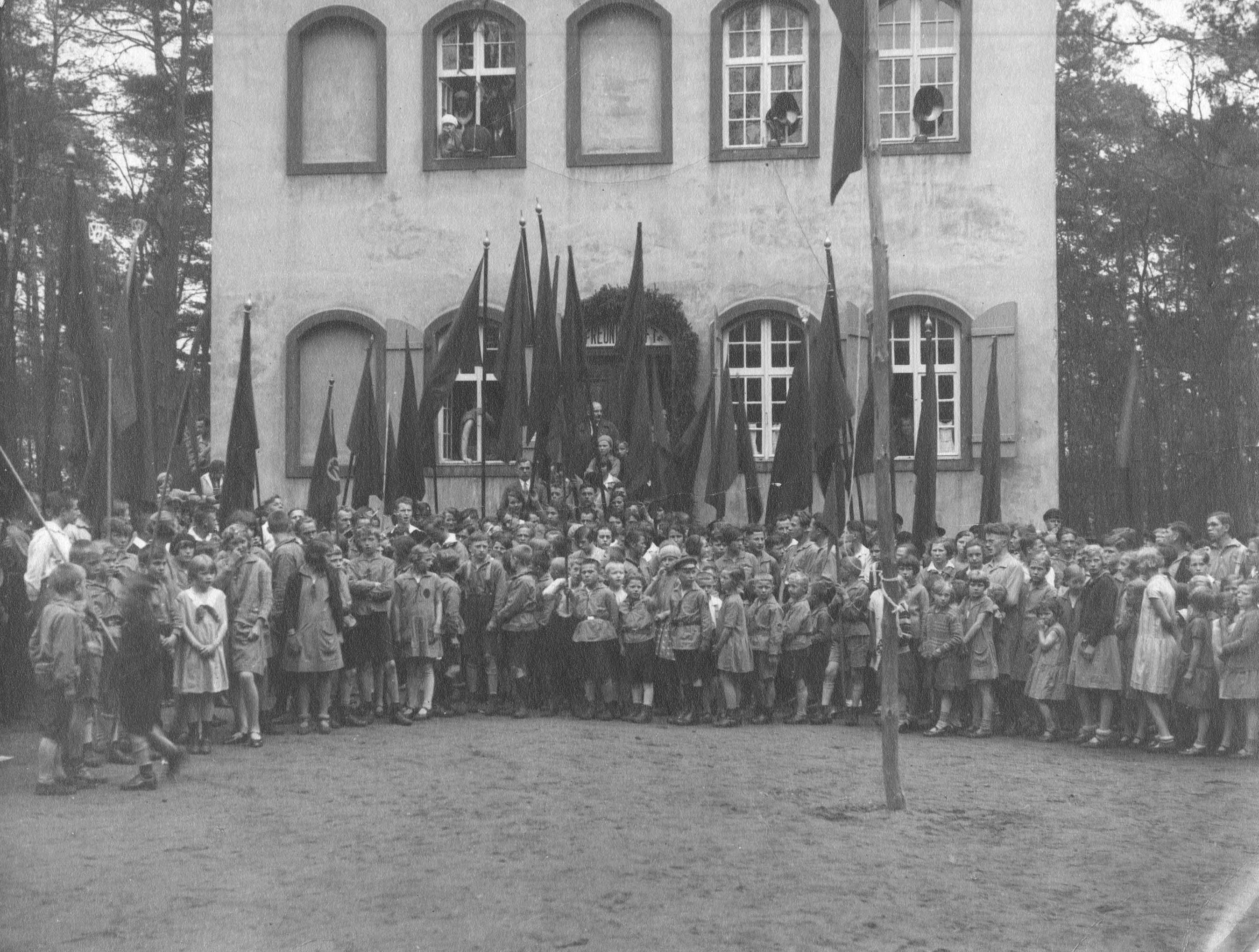 Schwarz-Weiß-Fotografie einer großen Gruppe von Kindern mit Fahnen bei einer Versammlung der Kinderfreunde vor einem Kinderfreundeheim, um 1925, ohne Ort. AdsD 6/FOTB016125.