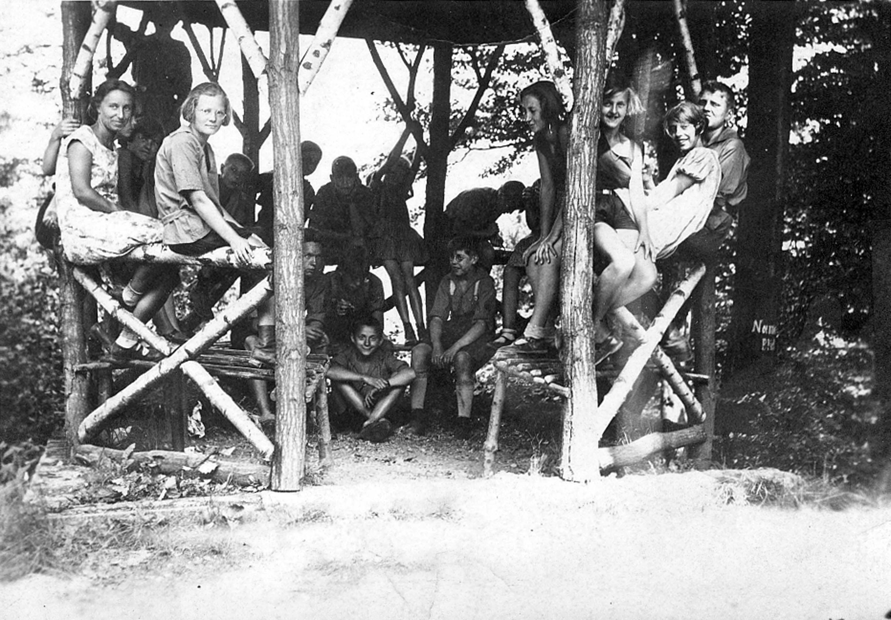 Schwarz-Weiß-Fotografie einer Kindergruppe in einem aus schmalen Baumstämmen gebauten Unterstand während der Kinderrepublik Namedy zwischen 1929 bis 1931. AdsD 6/FOTB016115.