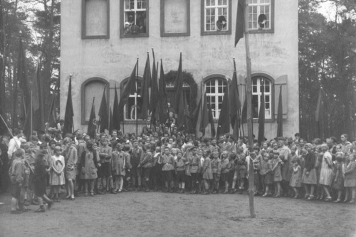 Schwarz-Weiß-Fotografie einer großen Gruppe von Kindern mit Fahnen bei einer Versammlung der Kinderfreunde vor einem Kinderfreundeheim, um 1925, ohne Ort. AdsD 6/FOTB016125.