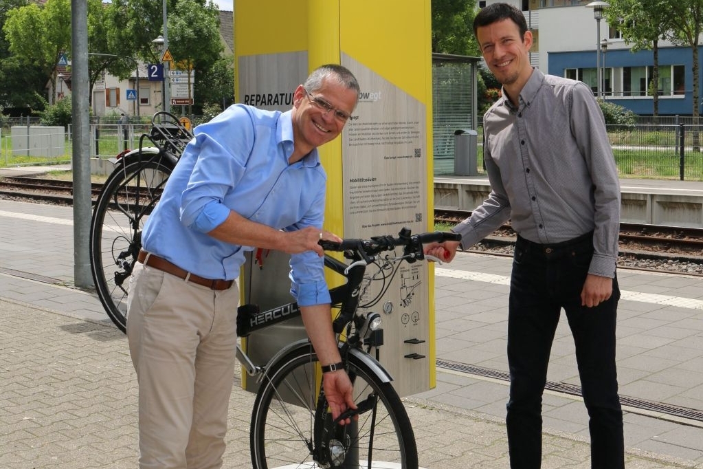 Bürgermeister Christoph Lipps und Stadtplaner Matthias Kaufhold (re.) vor einer Mobilitätssäule am Bahnhof Oberkirch, die über die Mobilitätsangebote informiert.