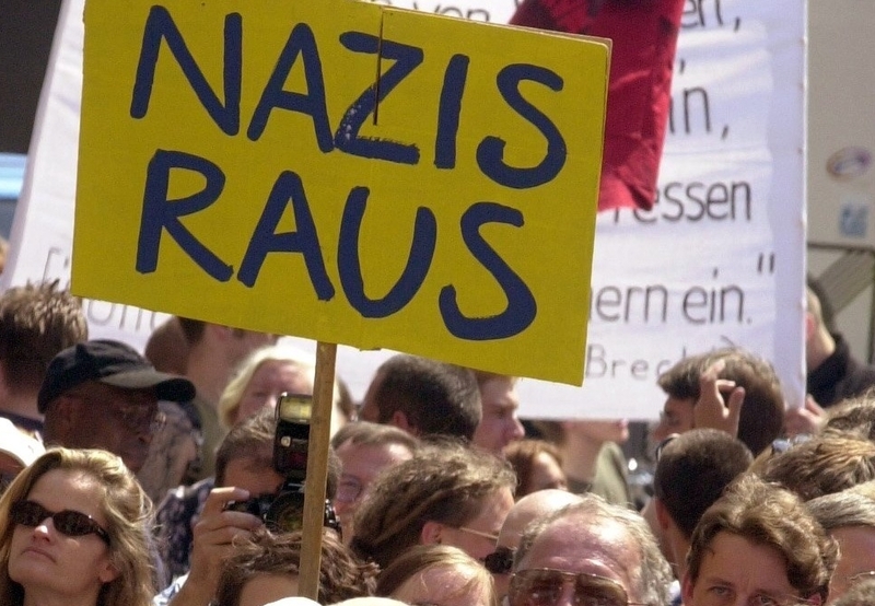 Demonstrierende Menschen. Auf einem Schild ist zu lesen: Nazis raus. Link zur Themenseite Gegen Rechtsextremismus.}