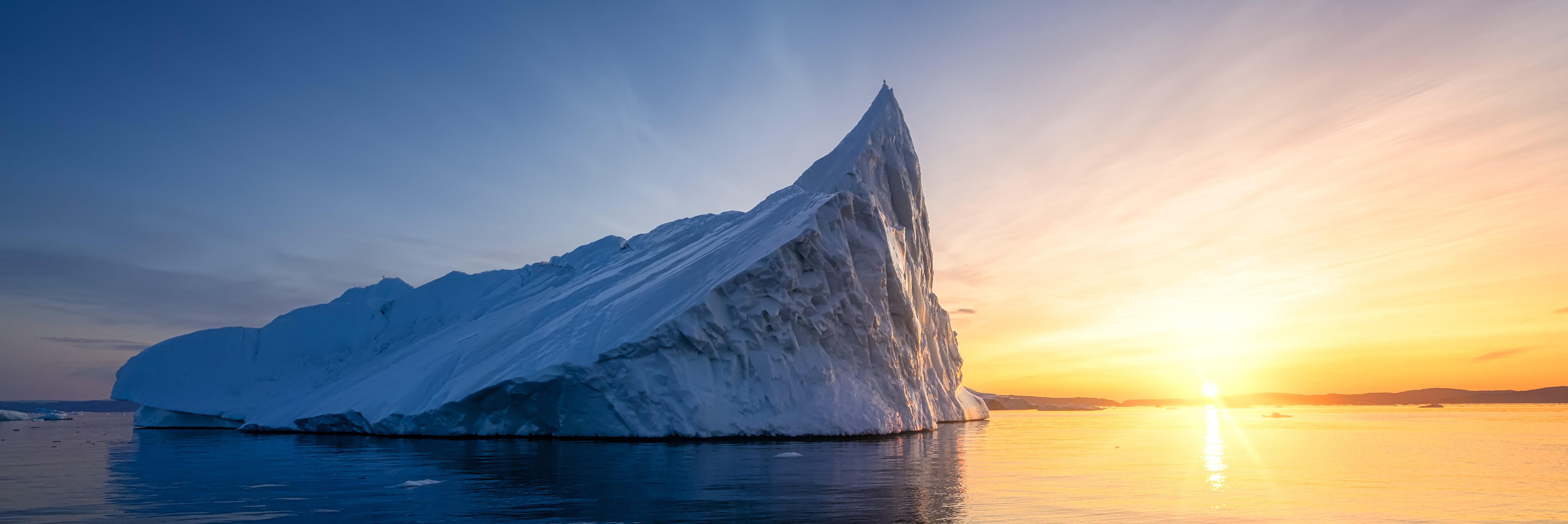 Eisberg im Meer, im Hintergrund ein Sonnenuntergang