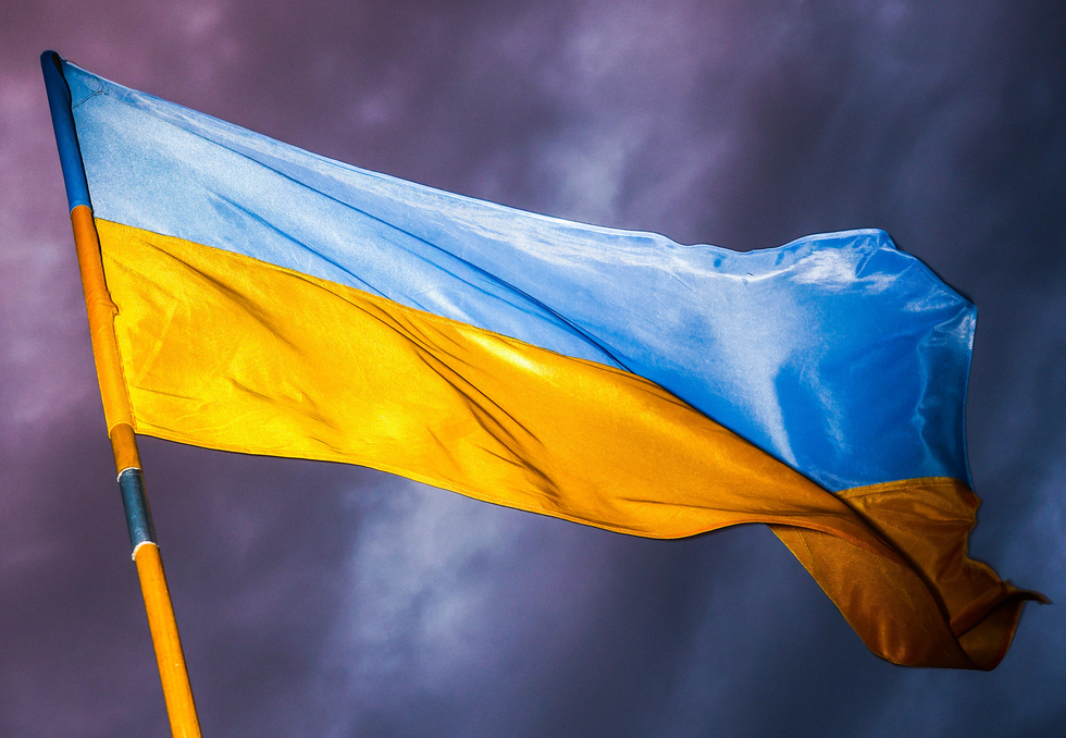 Wehende Ukraineflagge am Fahnenmast vor einem dunklen Hintergrund.
