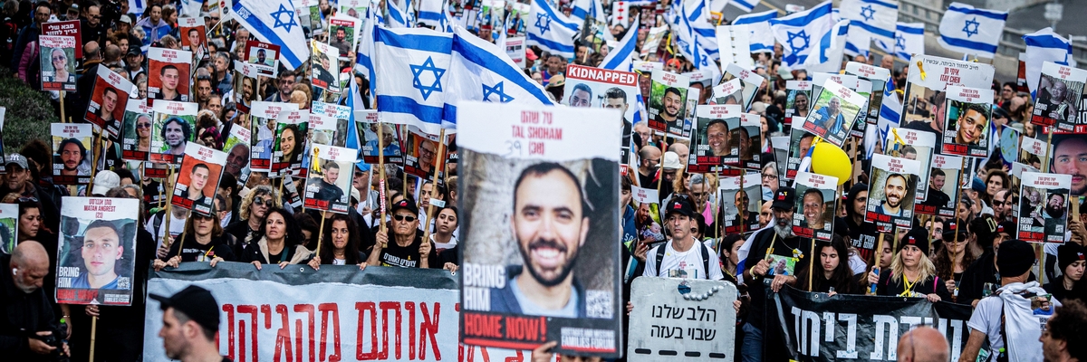 Demonstrationszug auf einer Straße mit vielen israelischen Flaggen und Plakaten mit Fotos der israelischen Geiseln mit der Aufschrift "Bring them home-now!"