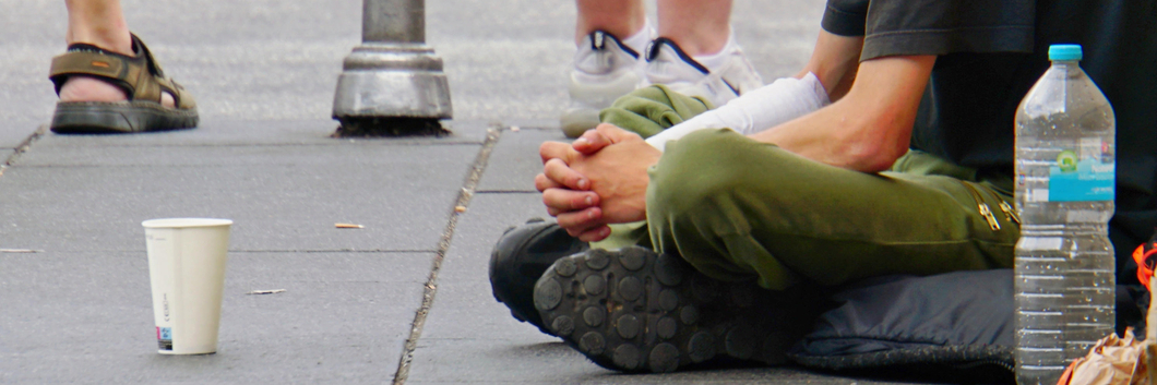 Eine Person sitzt bettelnd mit einem Becher auf der Straße.