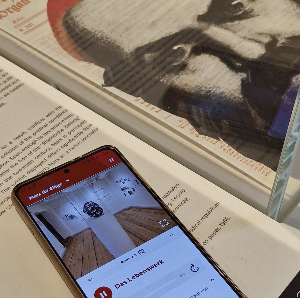 Ein Smartphone mit geöffneter Karl-Marx-Haus App liegt in der Ausstellung neben einem Bild von Karl Marx.