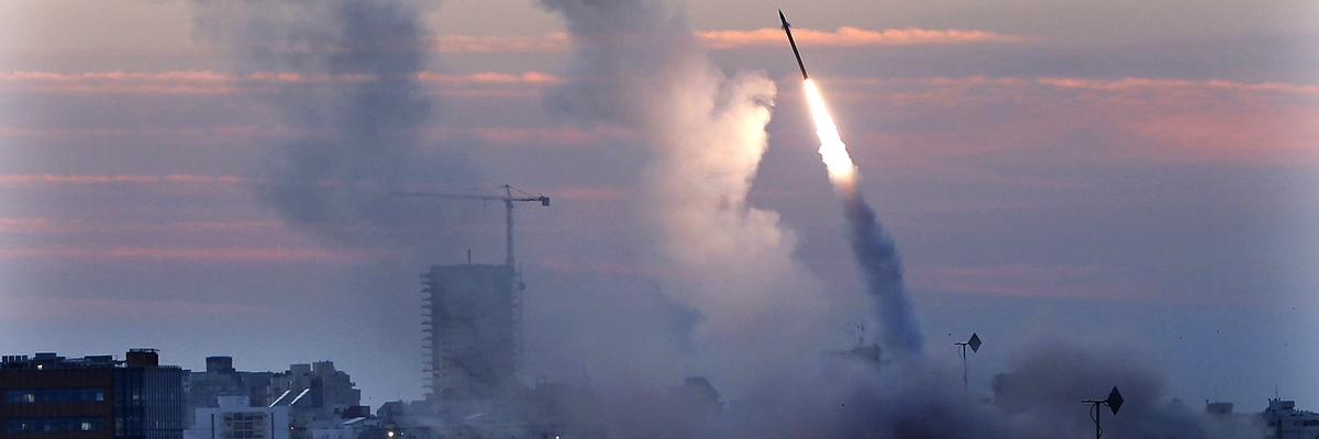 Ein Geschoss des israelischen mobilen Raketenabwehrsystem Iron Dome mit Feuerschweif und Rauch am Himmel über einem Wohngebiet. 