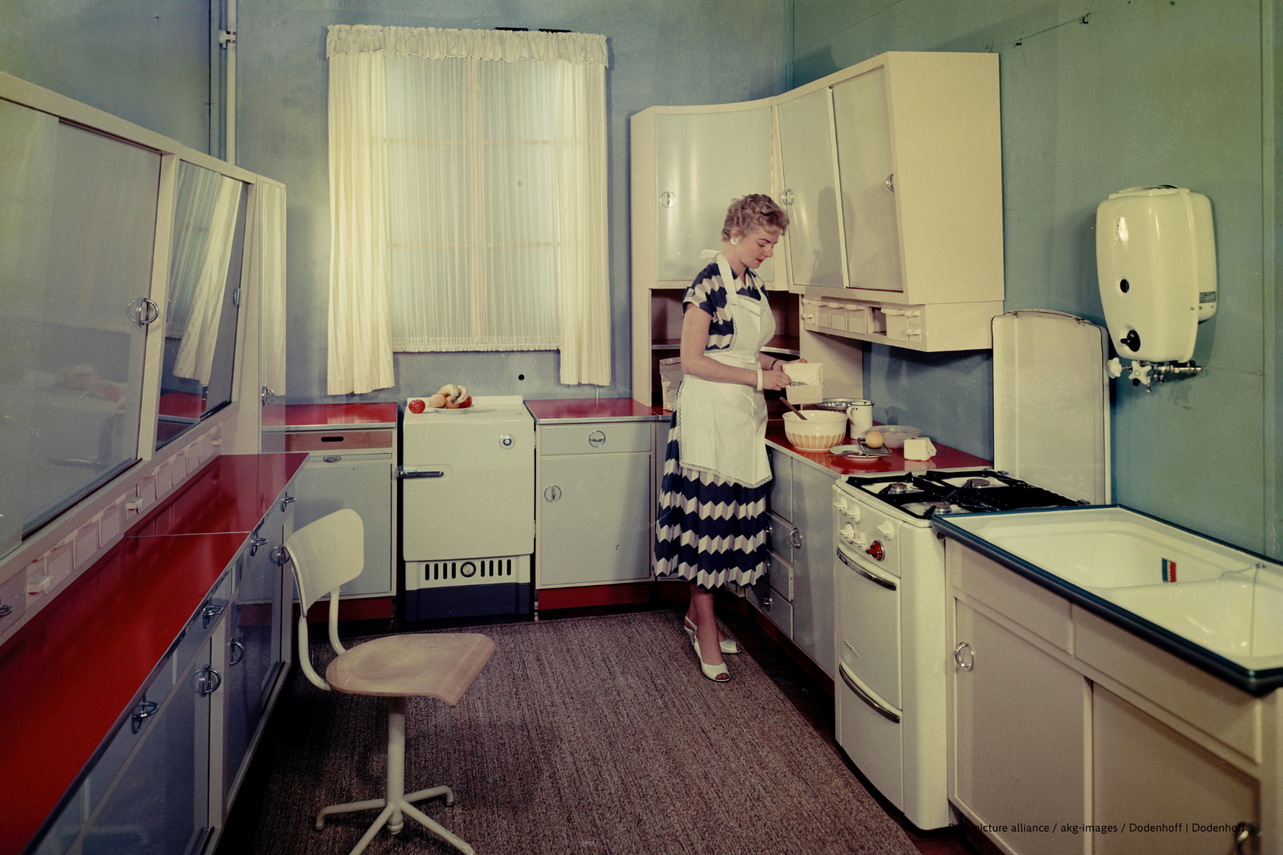 Wohnung / Küche: Hausfrau beim Backen in ihrer Einbauküche mit Gasherd und Gasboiler für die Warmwasserversorgung. Foto, um 1958.