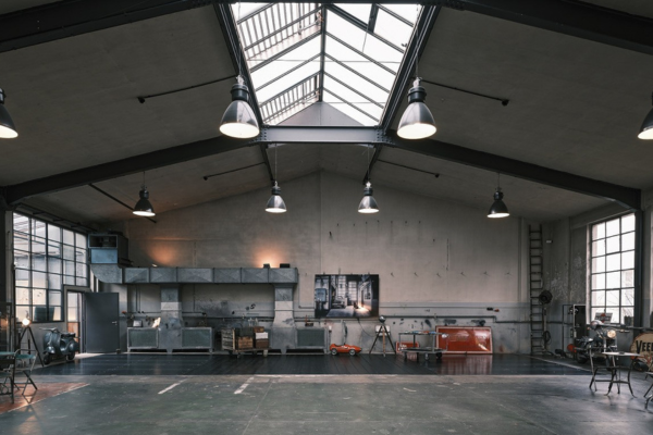 Große Industriehalle, früher wohl als Garage genutzt, mit großen Fenstern auf den Seiten und Oberlicht und einigen Sitzgelegenheiten