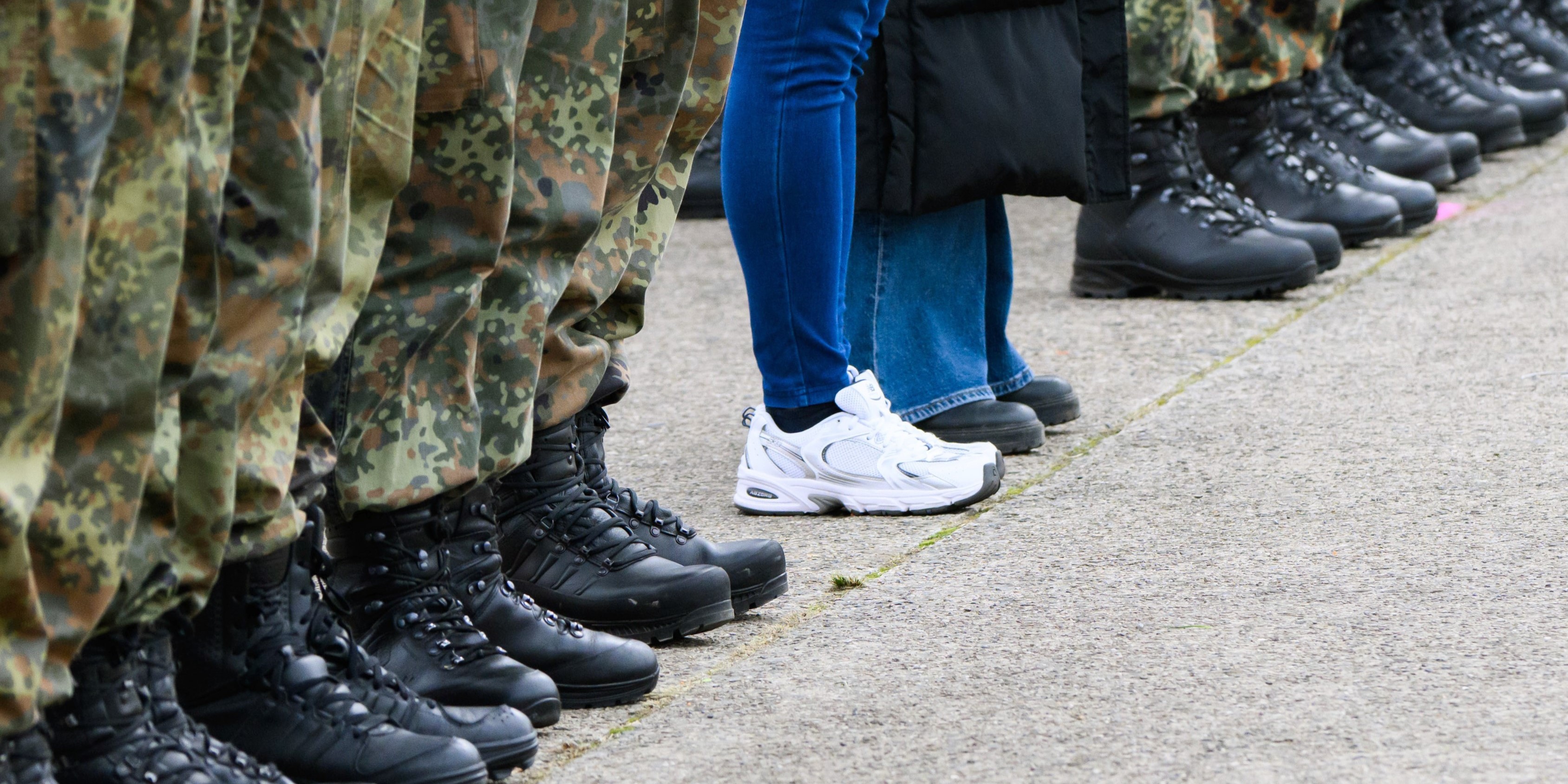 Eine Reihe Soldaten, daneben zwei Personen in zivil