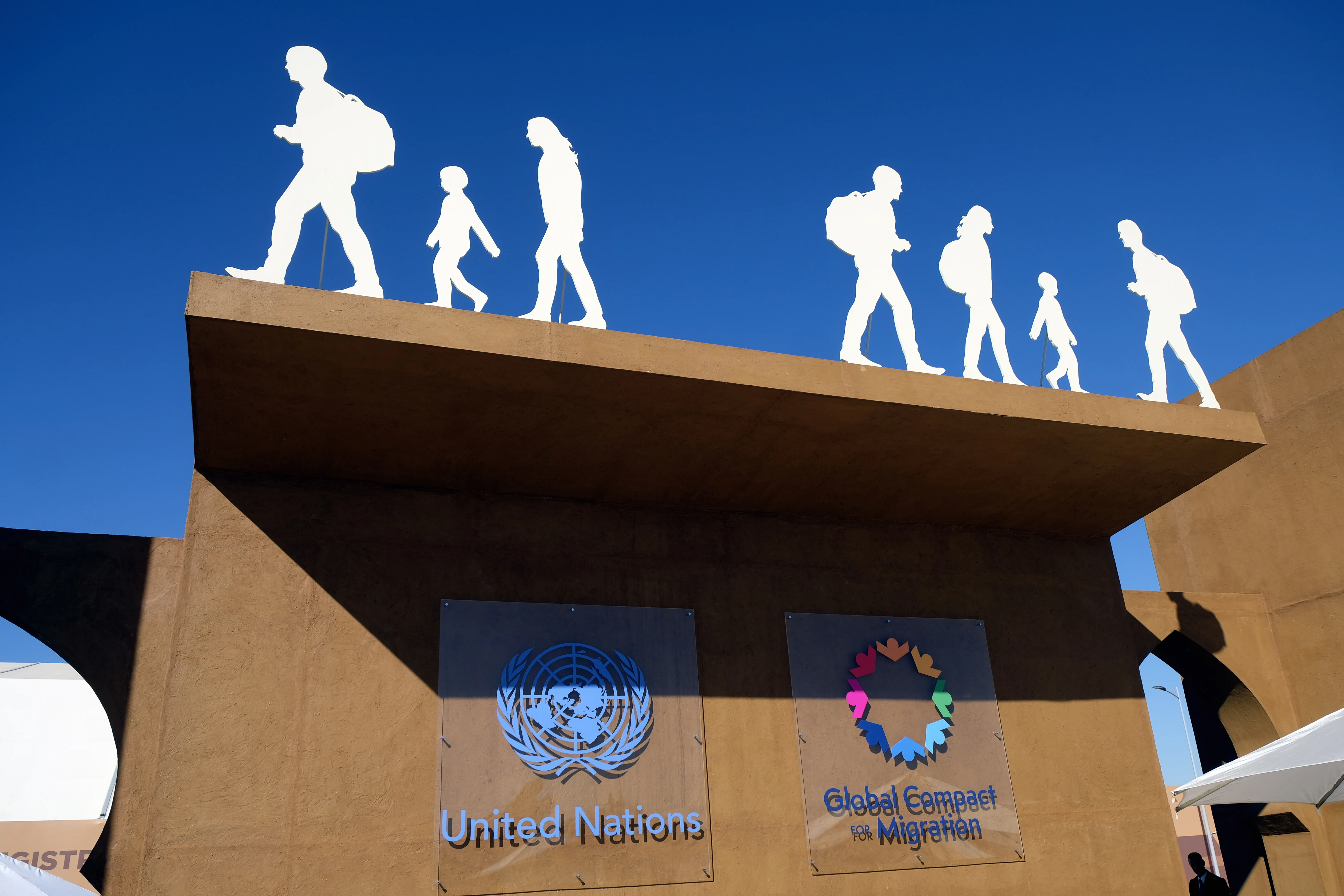Eingangsbereich die UN-Konferenz in Marrakesch, Marokko, zum Globalen Pakt der Vereinten Nationen für Migration mit UN Logo, GCM Logo und scherenschnittartige Personen auf dem Dach des Eingangsbereichs.