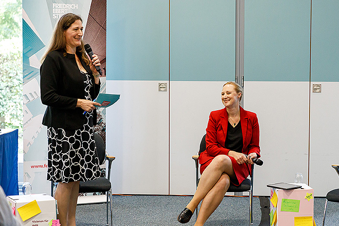 Anne Haller und Dörte Schall stehen vorm Plenum. Zu sehen ist außerdem das Banner der Kommunalakademie. 