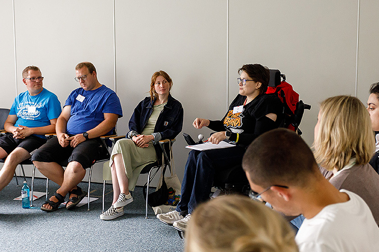 Seminarteilnehmer, eine Teilnehmerin im Rollstuhl andere sitzen daneben und hören zu, 