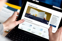 Webseite FES Digitales Lernen auf einem Bildschirm, der von zwei Händen getragen wird