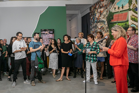 Sabine Fandrych Steht im Ausstellungsraum vor der Besuchergruppe und hält eine Rede.