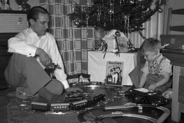 Ein Mann und ein Kind spielen mit einer Modelleisenbahn vor einem Weihnachtsbaum