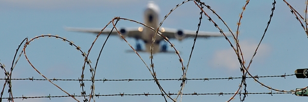 Ein Flugzeug startet von einem Flugfeld hinter Stacheldraht