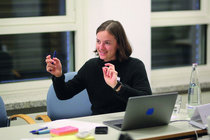 Trainerin Leonie Sontheimer sitzt an einem Tisch und erklärt den Teilnehmenden etwas.