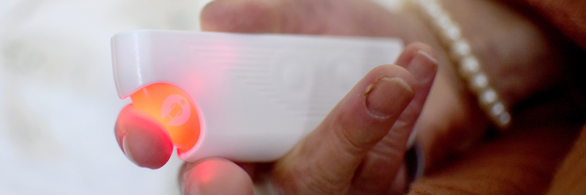 Eine ältere Hand hält einen Notfallknopf.