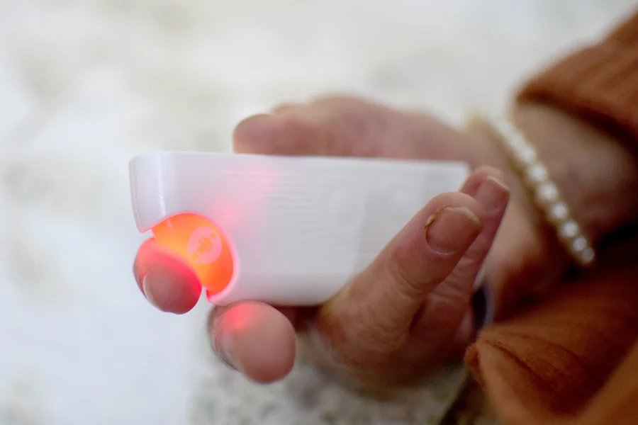 Eine ältere Hand hält einen Notfallknopf.