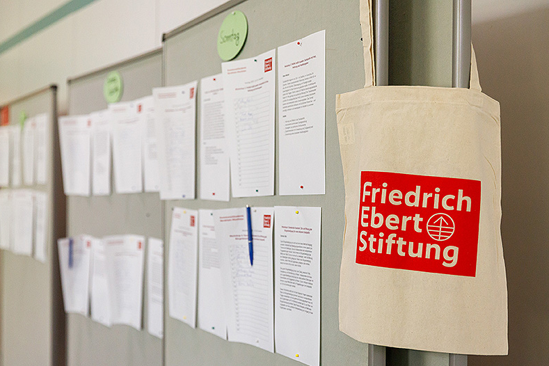 Pinnwand mit Aushang der Workshops. Tasche mit Friedrich Eberstiftung Logo. 