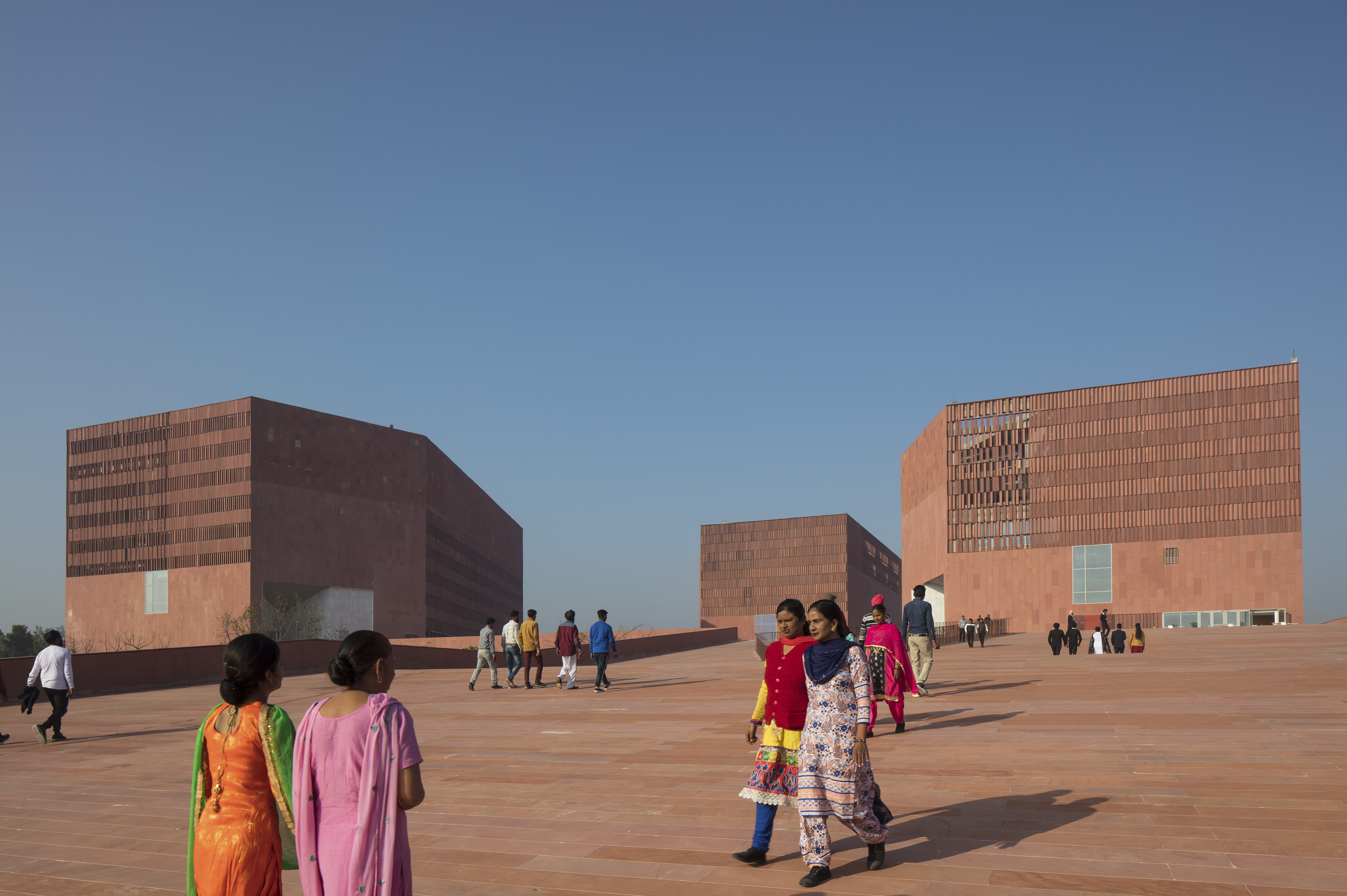 Footpath on the campus of Thapar University, Patiala, India, with students in front of a very modern building designed by McCullough Mulvin Architects, against a blue sky. 