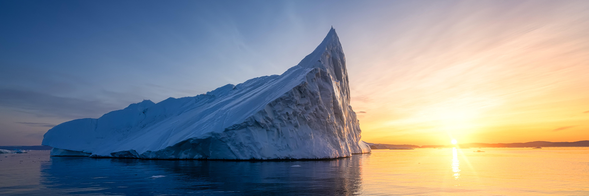 Ein Eisberg im Meer, im Hintergrund geht die Sonne unter.