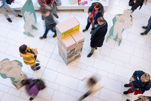 Blick von oben auf Elemente der FES-Wohnraumausstellung und auf Menschen, die sie gerade betrachten und sich durch den Raum bewegen