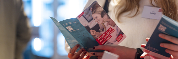 Der Programmflyer der Journalist:innen-Akademie der FES mit der Aufschrift "Kompetenzen für den Journalismus von morgen" wird von einer jungen Frau gelesen.