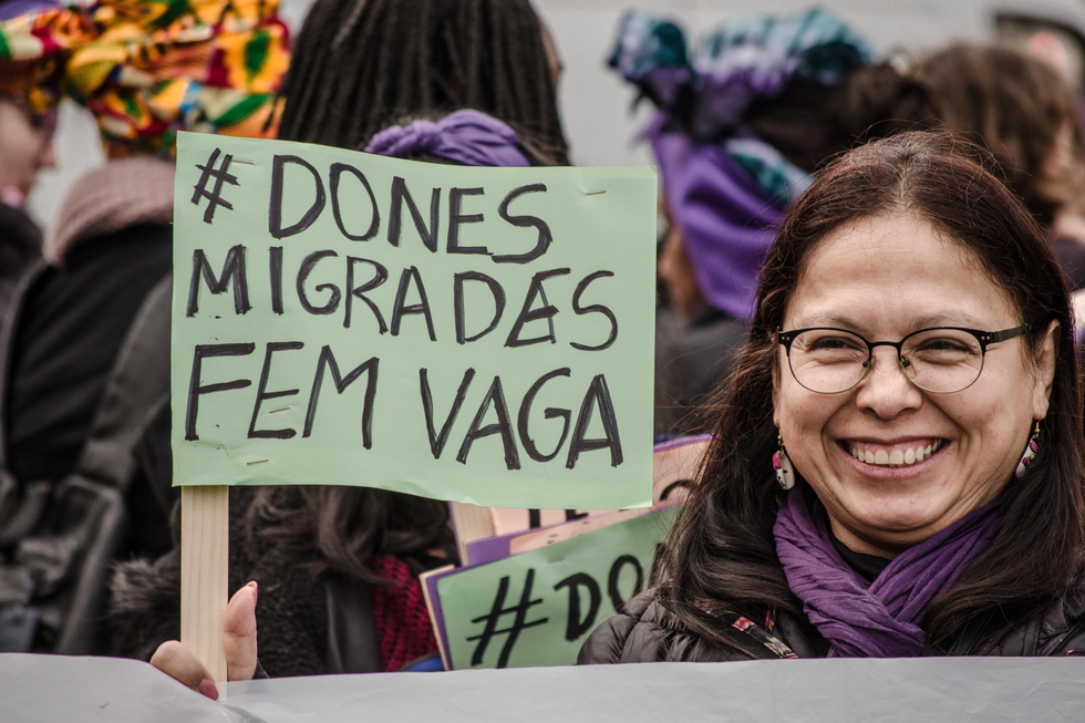 Eine Demonstrantin zeigt ein Plakat, das sich auf streikende Migrantinnen bezieht. Auf dem Plakat steht "Dones Migrades Fem vaga", "Migrantinnen in Bewegung".